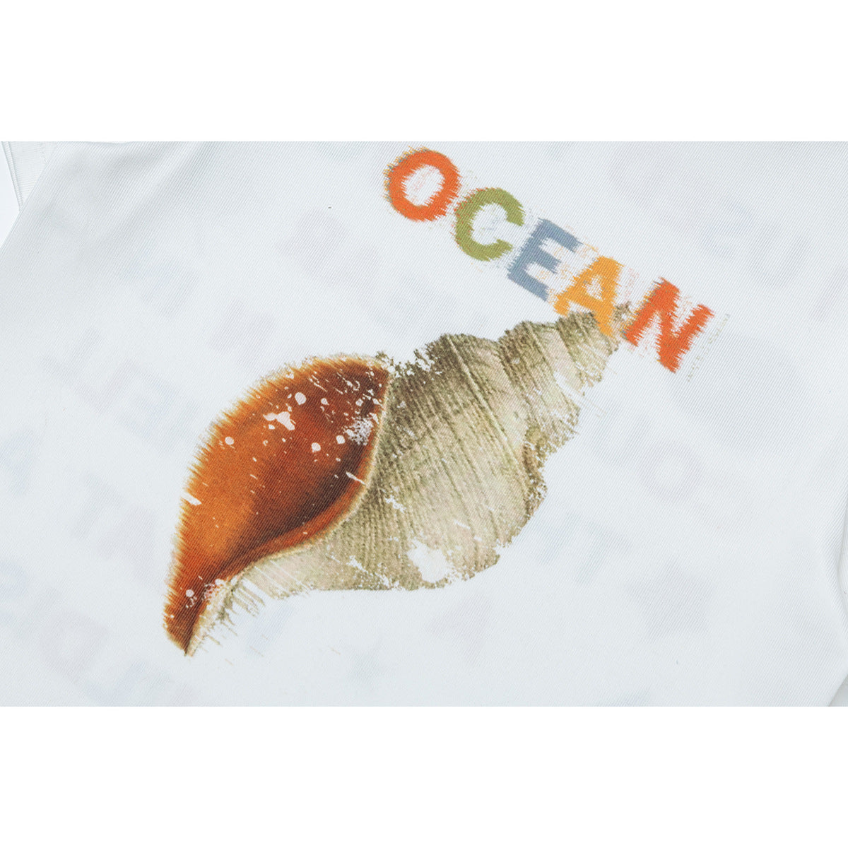 Close-up of a multicolored seashell graphic and the word “OCEAN” printed on a white T-shirt.