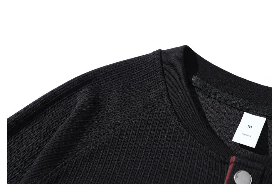 Close-up of the black ribbed top's collar and raglan shoulder seam, with a visible M size tag.