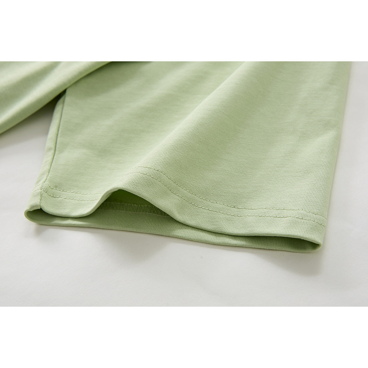 Close-up of the double-stitched hem on a pale green T-shirt.