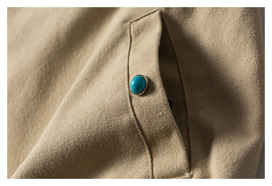 Close-up of a turquoise button on a flap of beige textured garment fabric.