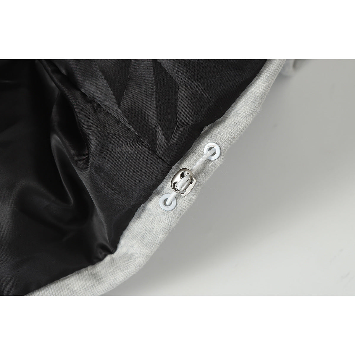 Close-up of the jacket's black lining and a white drawcord threaded through metal grommets in the gray edge.