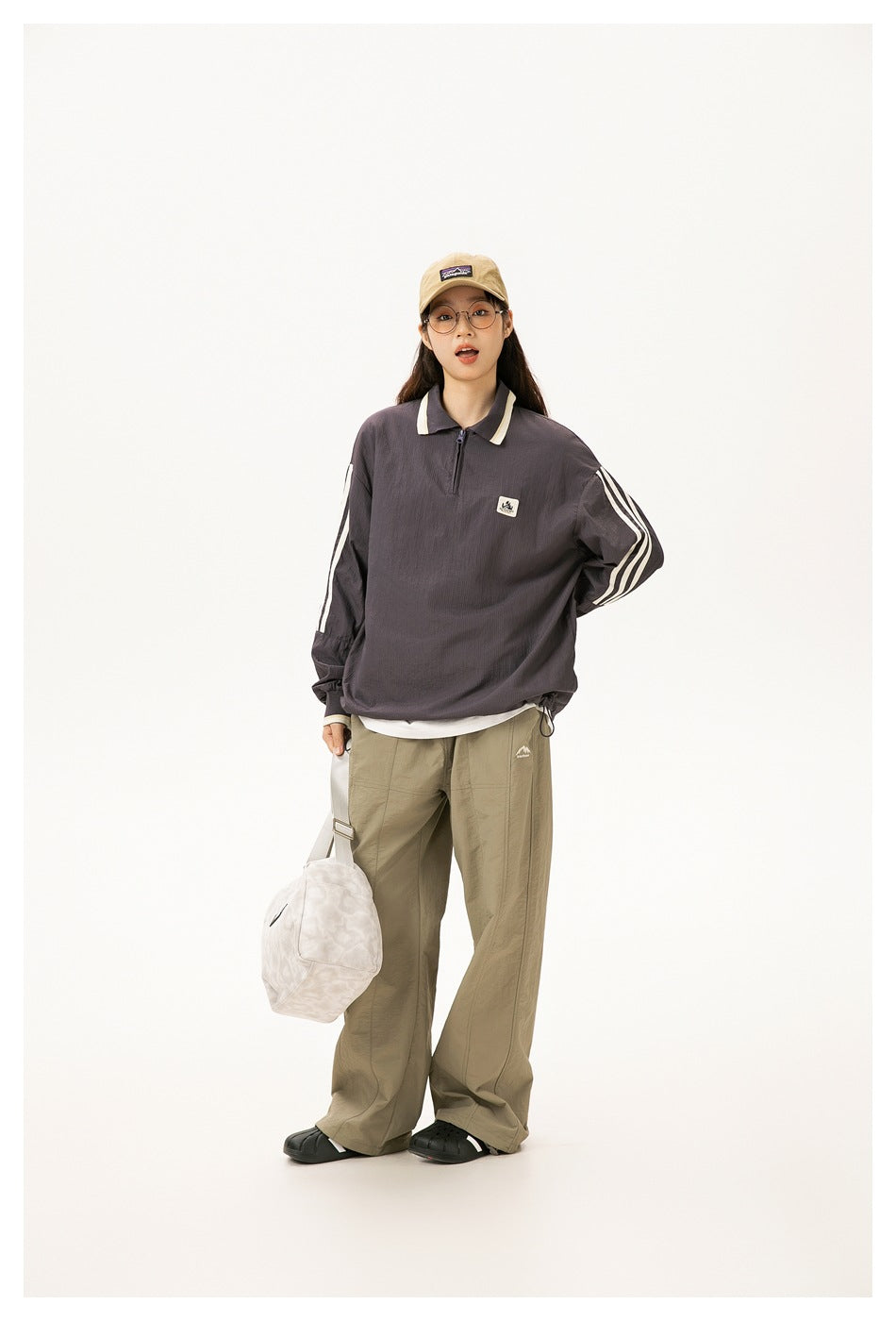 Model poses in a charcoal oversized quarter-zip pullover with cream collar trim and striped sleeves.