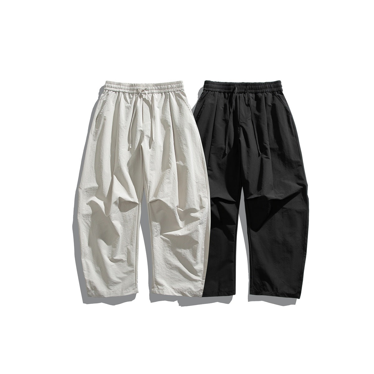 Front view of loose, tapered drawstring pants in cream and black, shown side by side.
