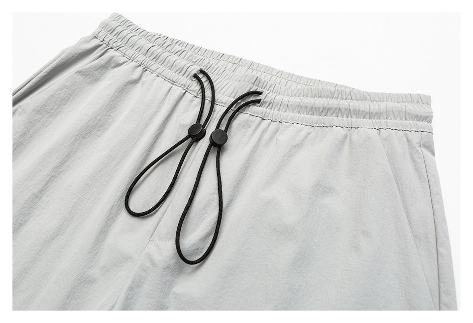 Close-up of light gray pants with an elastic waistband and black drawcords with round toggles.