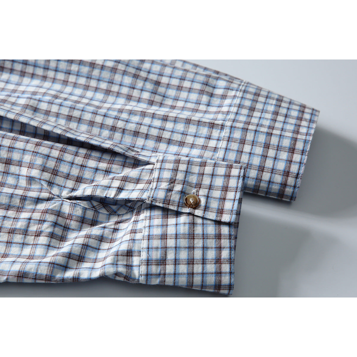 Close-up of the blue-and-brown plaid shirt's long sleeve and cuff with a brown button.