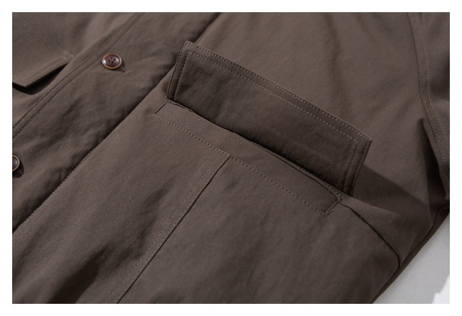 Close-up of a dark brown coat's rectangular pocket and buttoned flap.