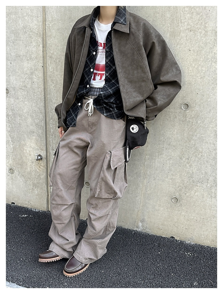 Model wearing a dark brown zip jacket over a plaid shirt with loose taupe cargo trousers.