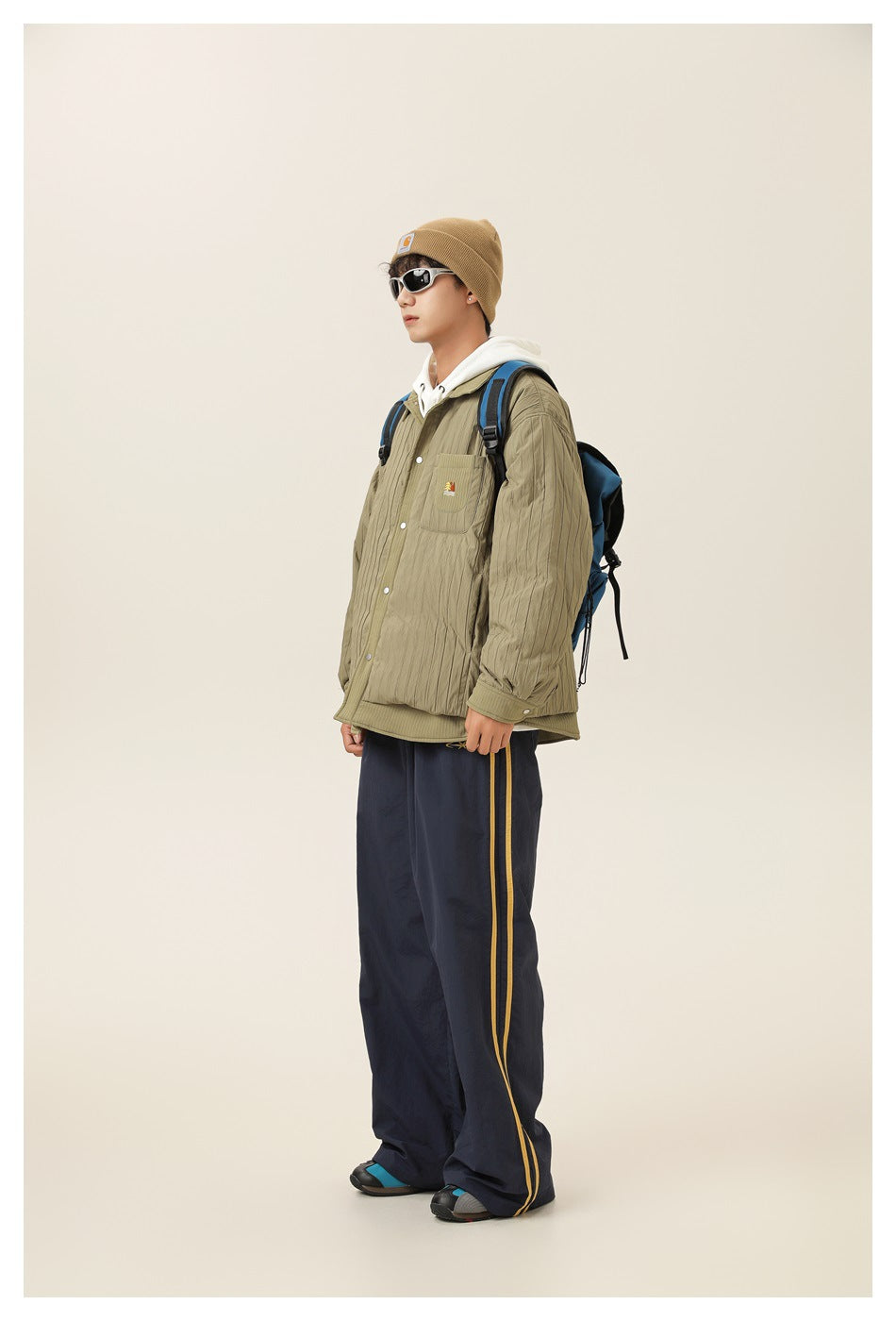 A model in profile wears an olive quilted jacket with a chest pocket and a white hooded layer.