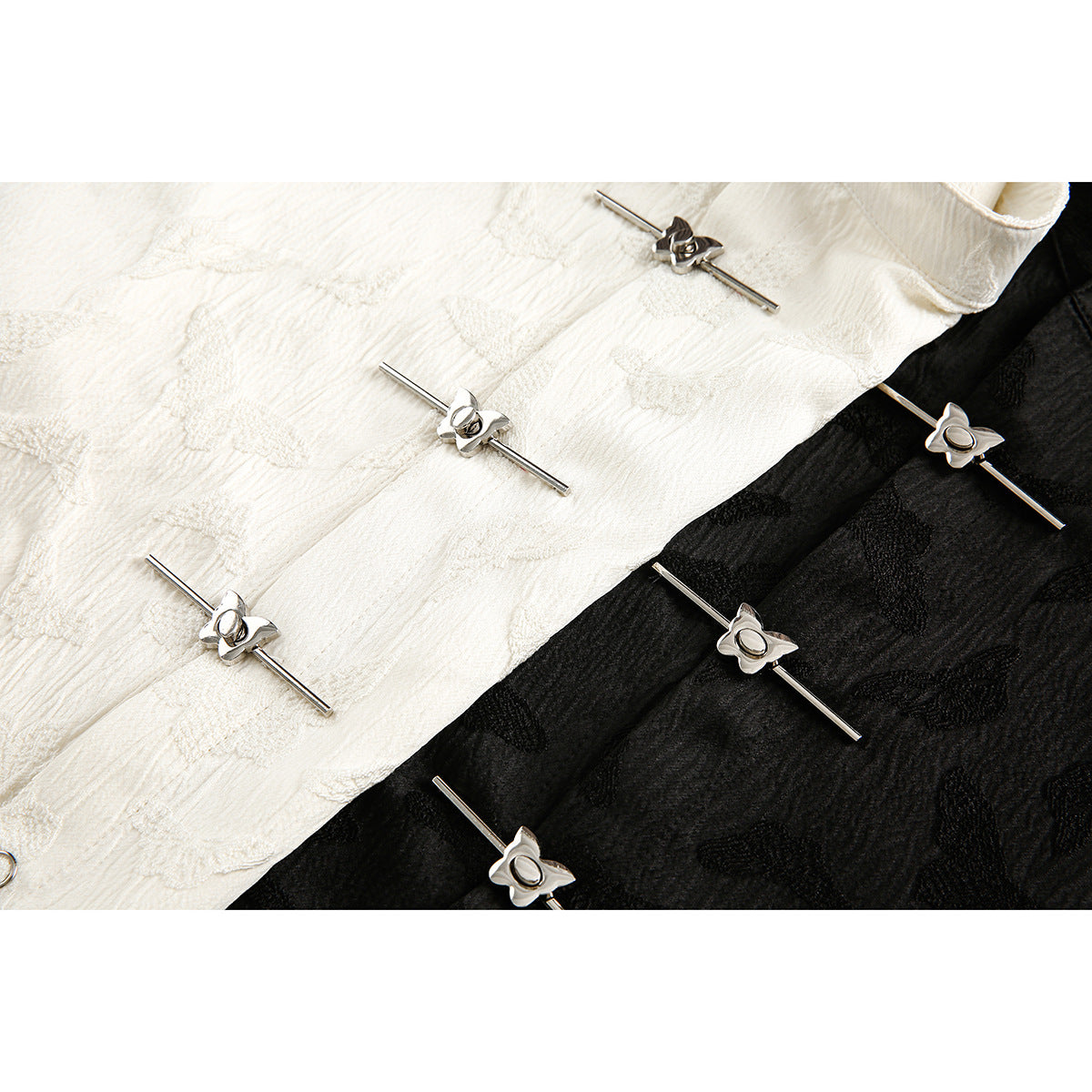 Close-up of silver flower-shaped bar closures on white and black textured shirt fabric.