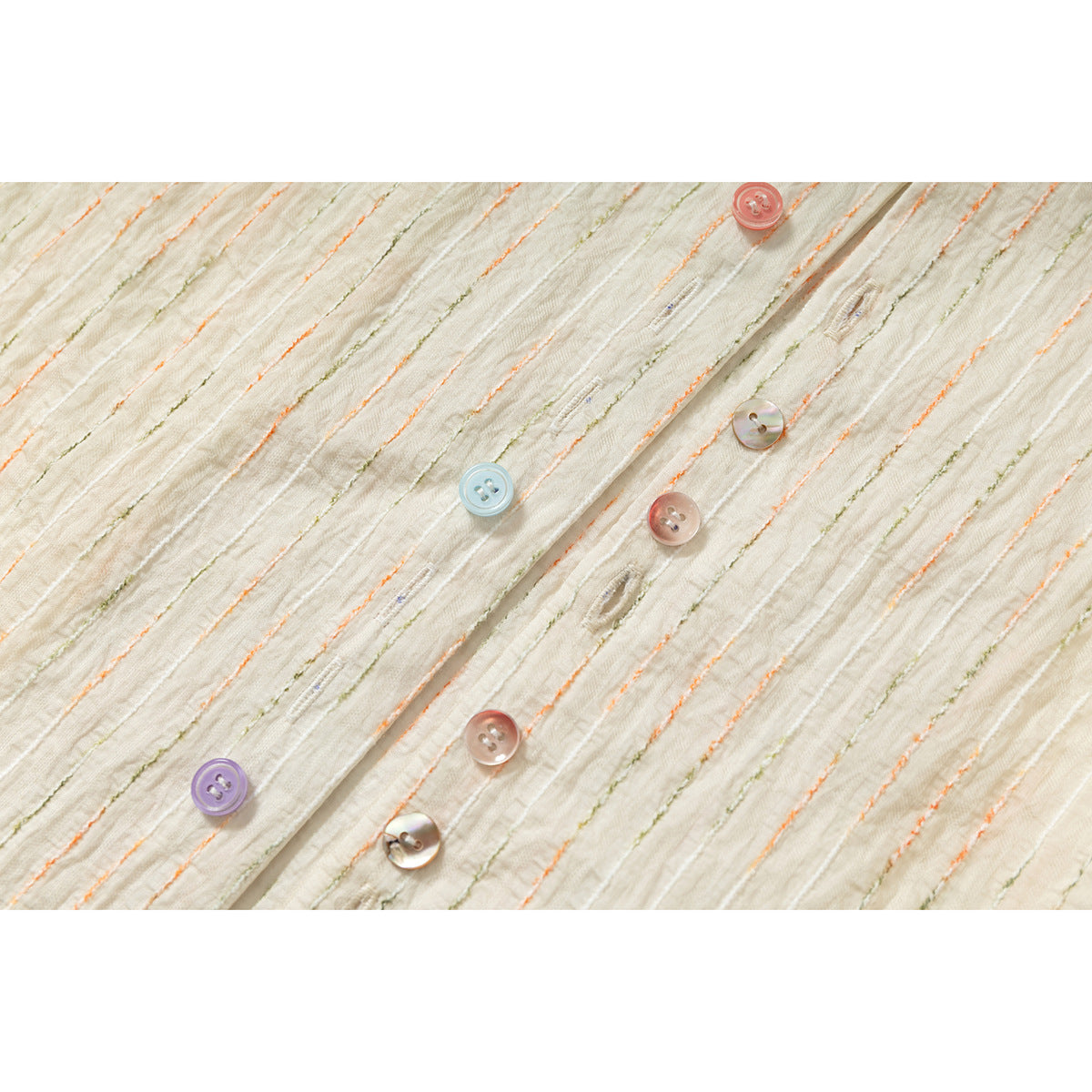 Close-up of the ivory shirt's textured, striped fabric and placket with assorted pastel buttons.