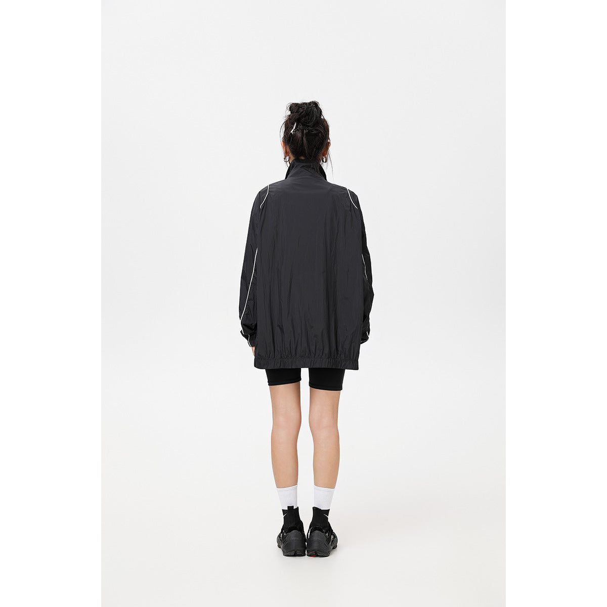 Back view of a model wearing a black jacket with white piping and a gathered hem.