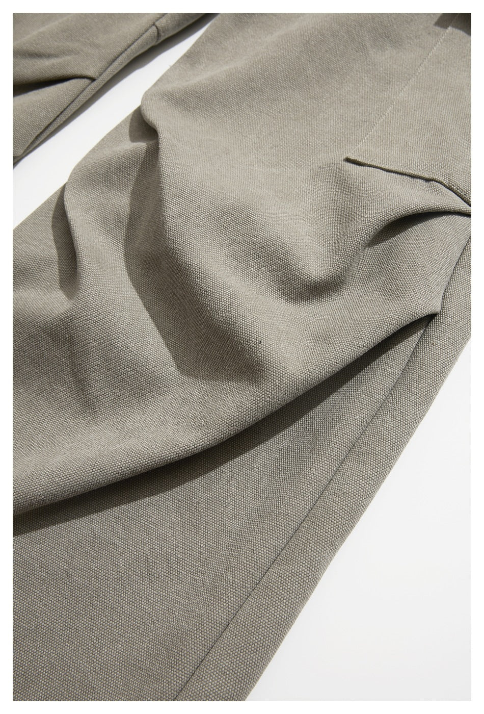 Close-up of taupe-gray trouser fabric, seams and a narrow pocket opening.