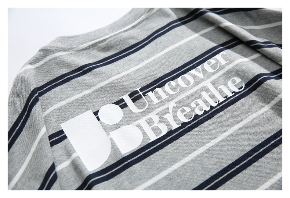 Close-up of a heather gray shirt with navy and white stripes and large white “Uncover Breathe” lettering.