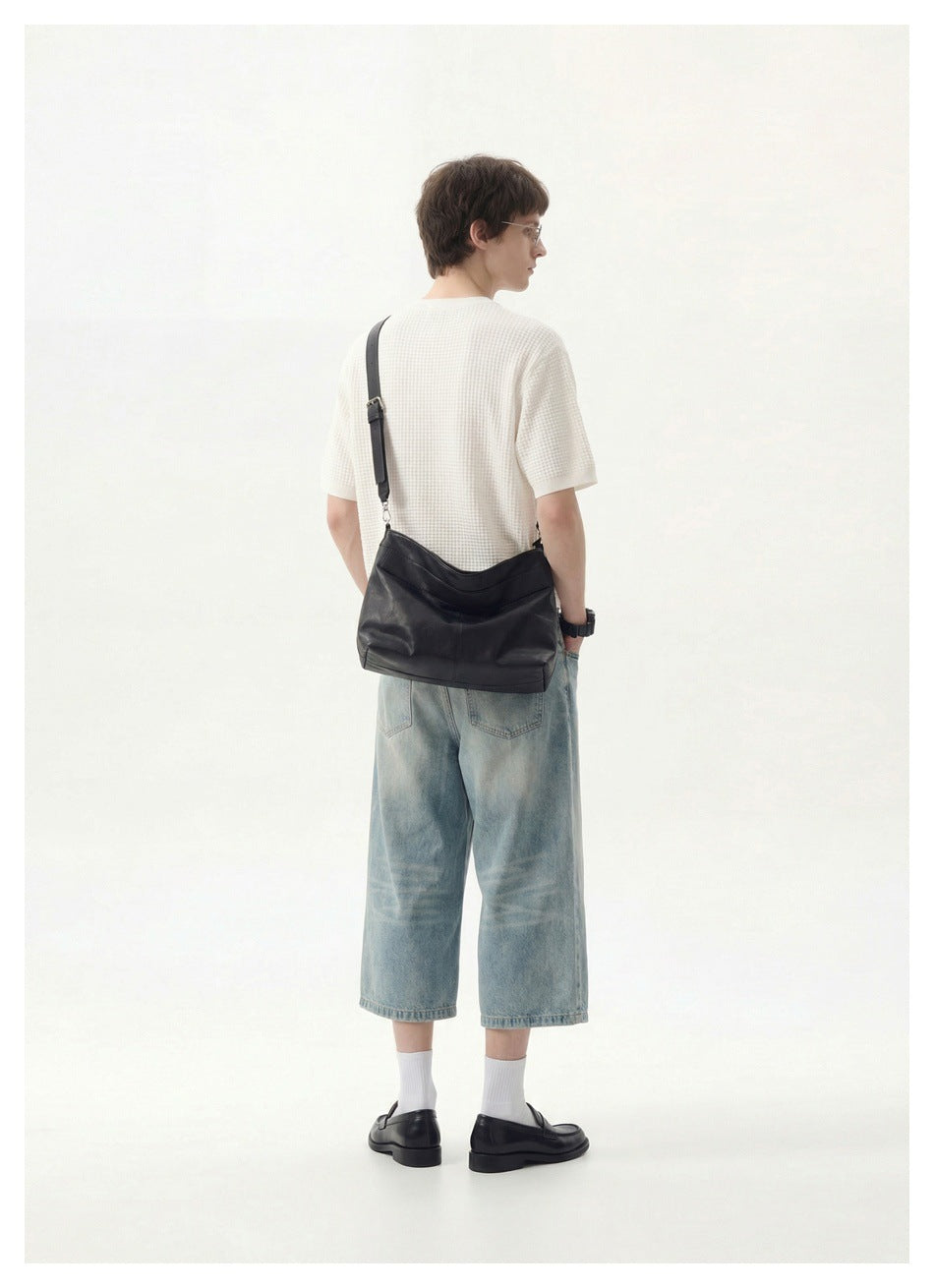 Rear view of a model in a white textured short-sleeve shirt and light-wash denim shorts, carrying a black shoulder bag.