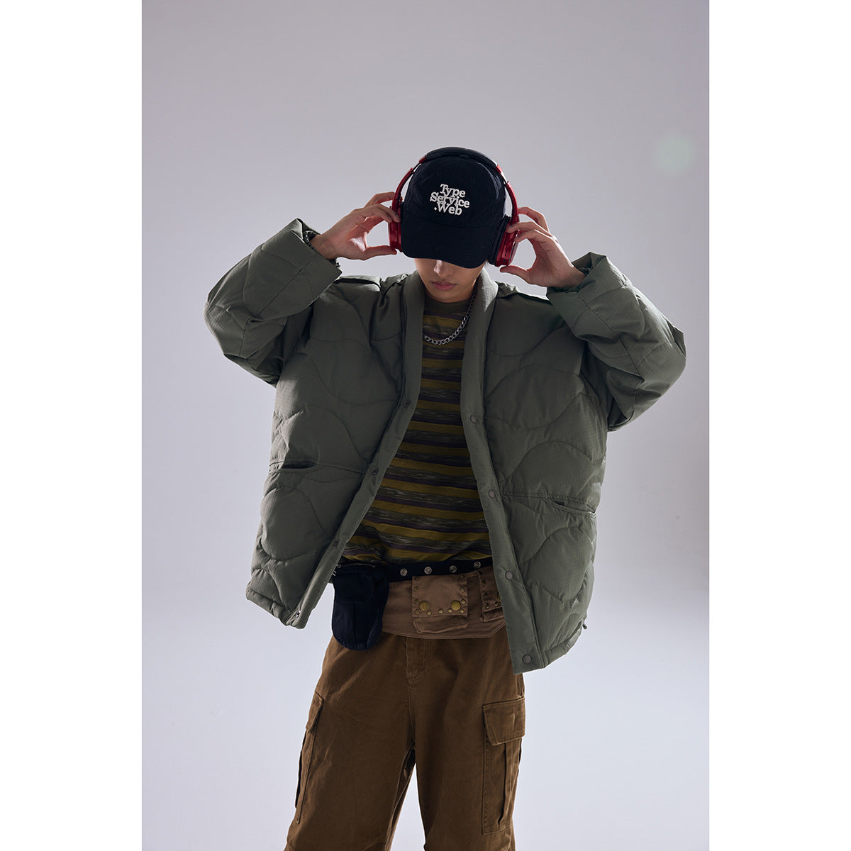 Model wearing an olive quilted button-front jacket, shown from the front with hands raised near the headphones.