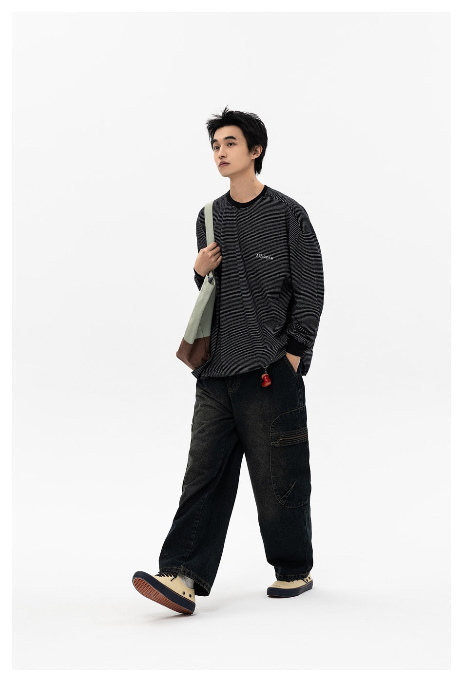 Man wearing a black thin-striped long-sleeve shirt with dark loose jeans and carrying a shoulder bag.