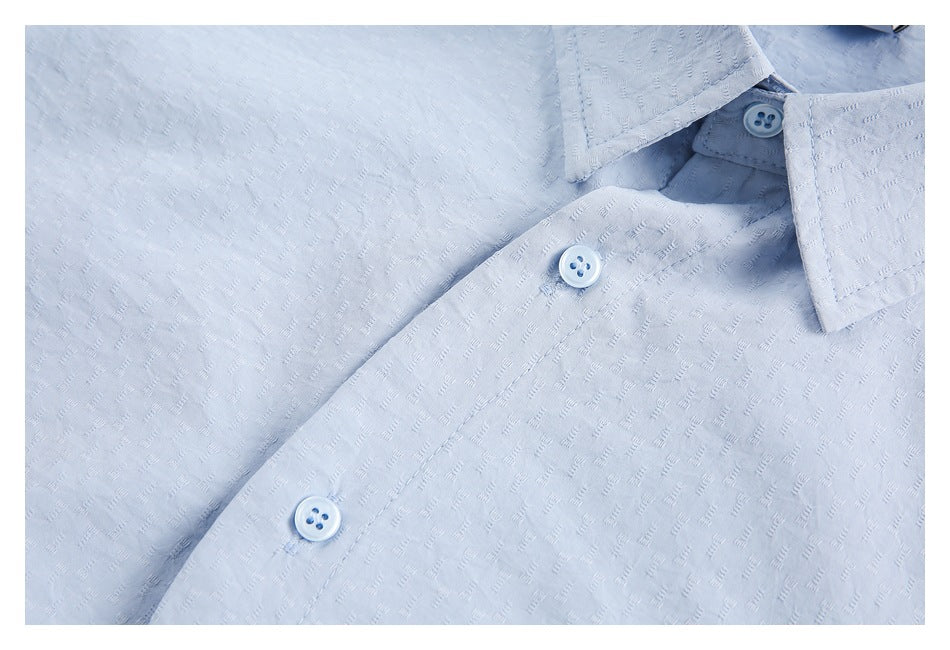 Close-up of a light blue shirt's textured fabric, collar edge, and button placket.