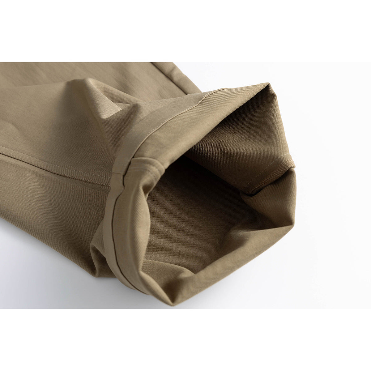 Close-up of the folded hem and stitched seam of taupe trousers.