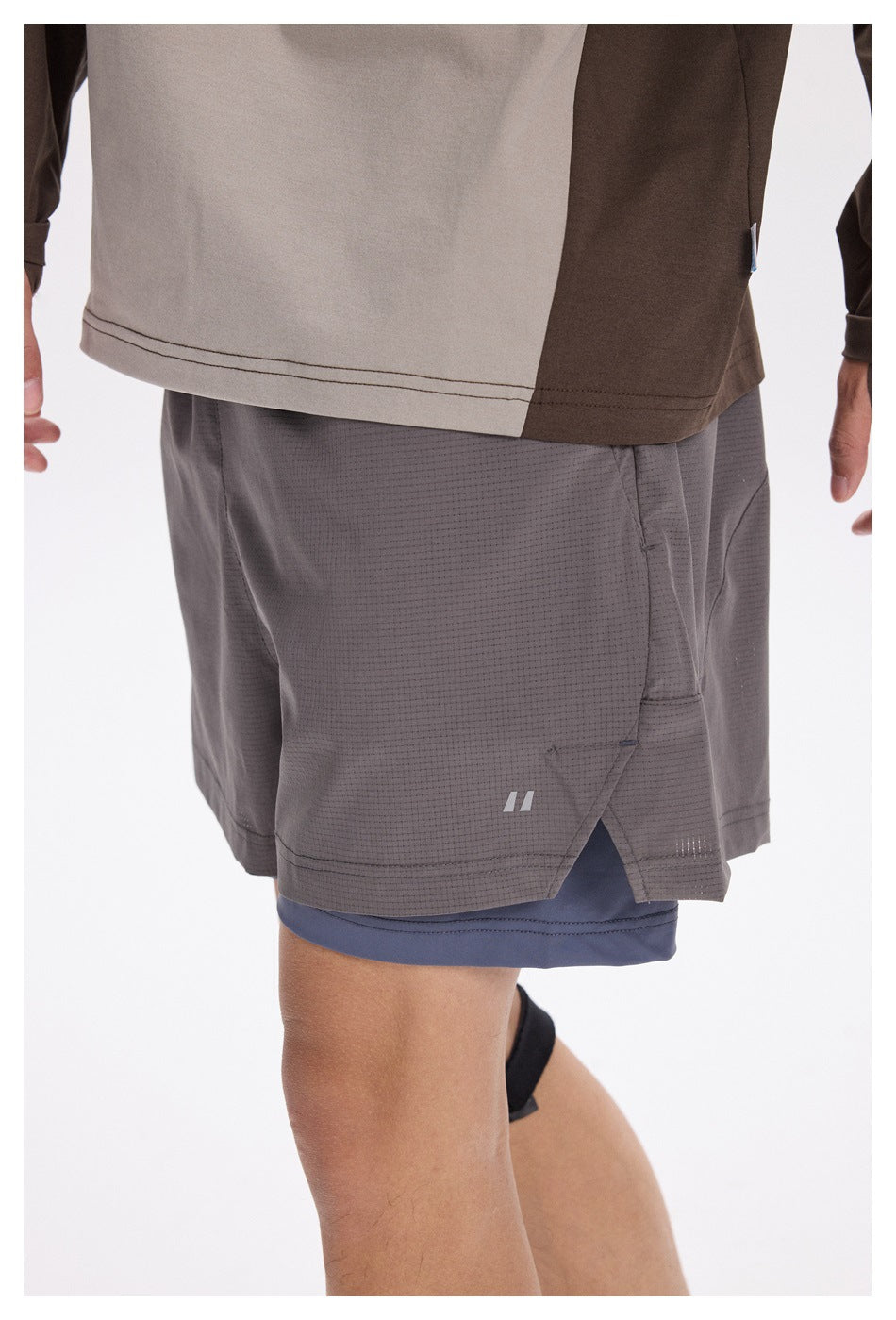 Close detail of gray running shorts layered over blue-gray compression shorts, showing the side slit and small logo.