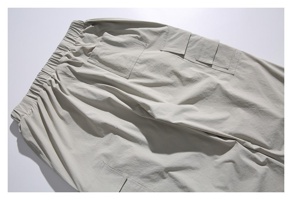 Partial flat lay of light gray-beige cargo trousers with an elastic waist and several flap pockets.
