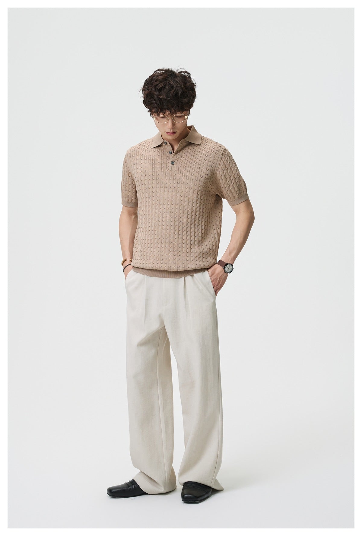 Man wearing beige wide-leg pleated trousers with a tan knit polo and black loafers, front view, hands in pockets