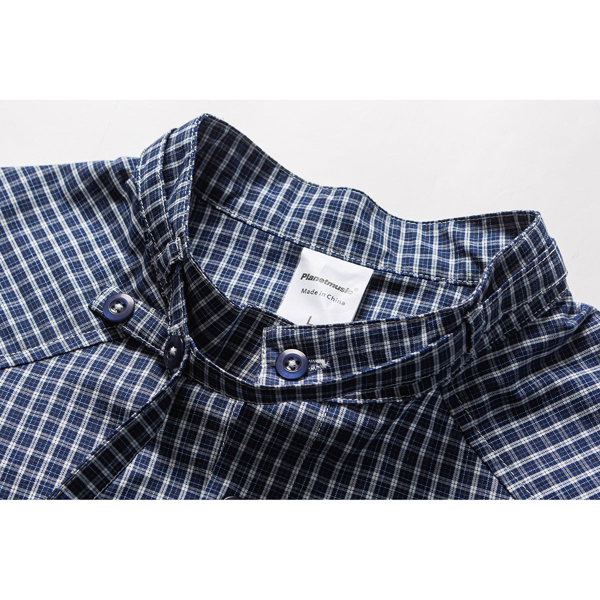 Close-up of a navy, white, and gray plaid shirt collar with dark buttons and an English neck label.