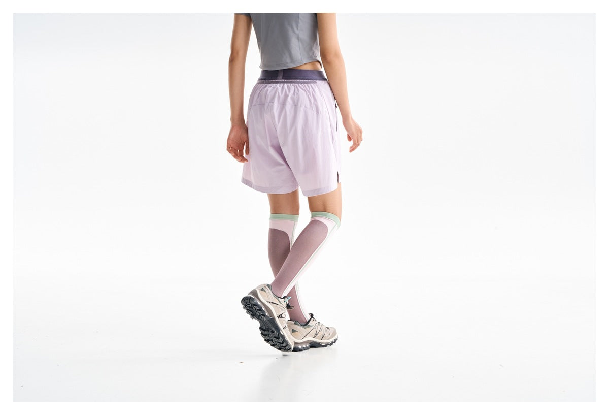 Cropped rear view of a model wearing lilac shorts with a dark waistband and pink knee-high socks.