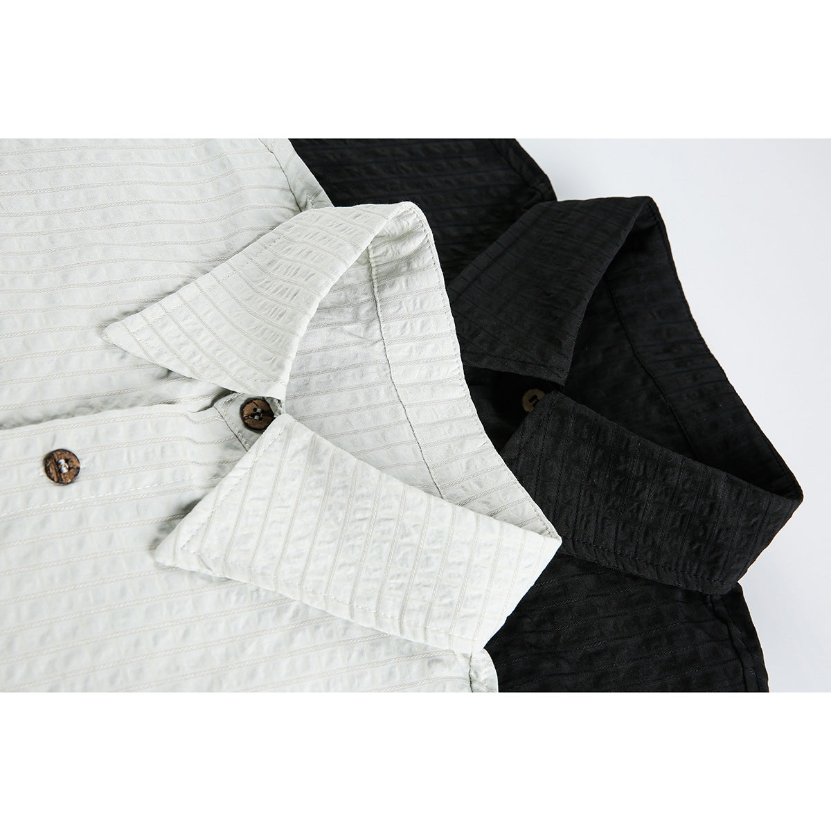 Close-up of white and black shirts showing pointed collars, short sleeves, textured stripes, and brown buttons.
