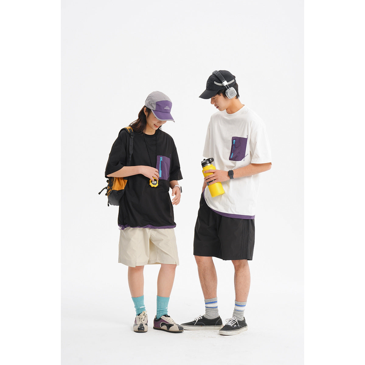 Two models wearing oversized black and white T-shirts with purple zip chest pockets and contrasting shorts.