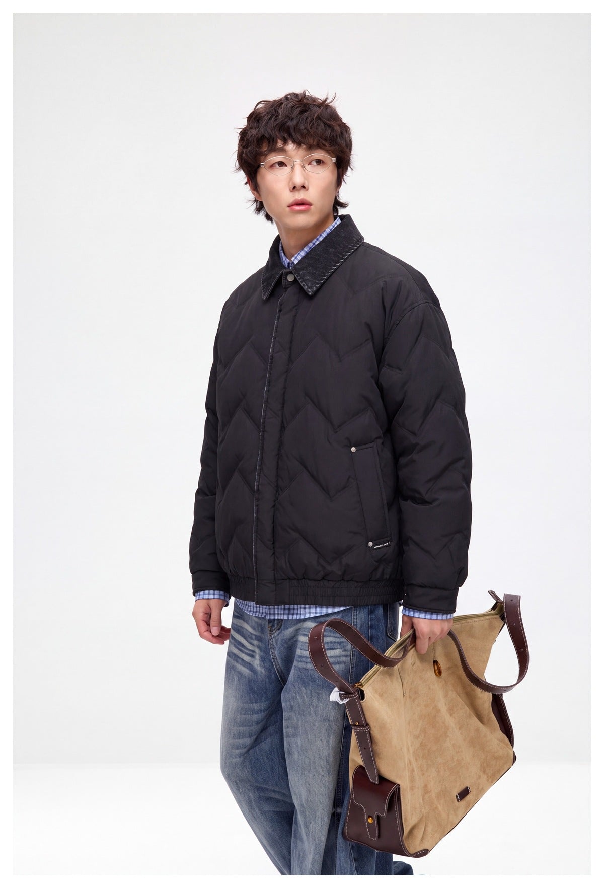 Model wearing a dark chevron-quilted jacket with a pointed contrast collar and front pockets over a blue gingham shirt.