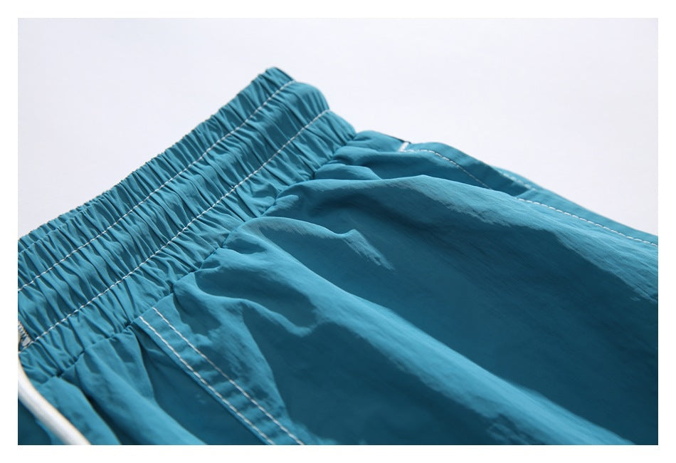 Close-up of teal shorts showing the gathered elastic waistband and white contrast stitching.