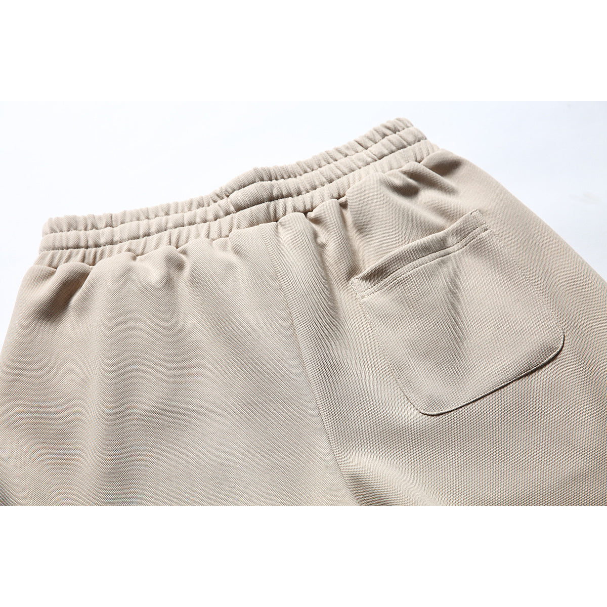 Close-up of the beige shorts' elastic back waistband and patch pocket.