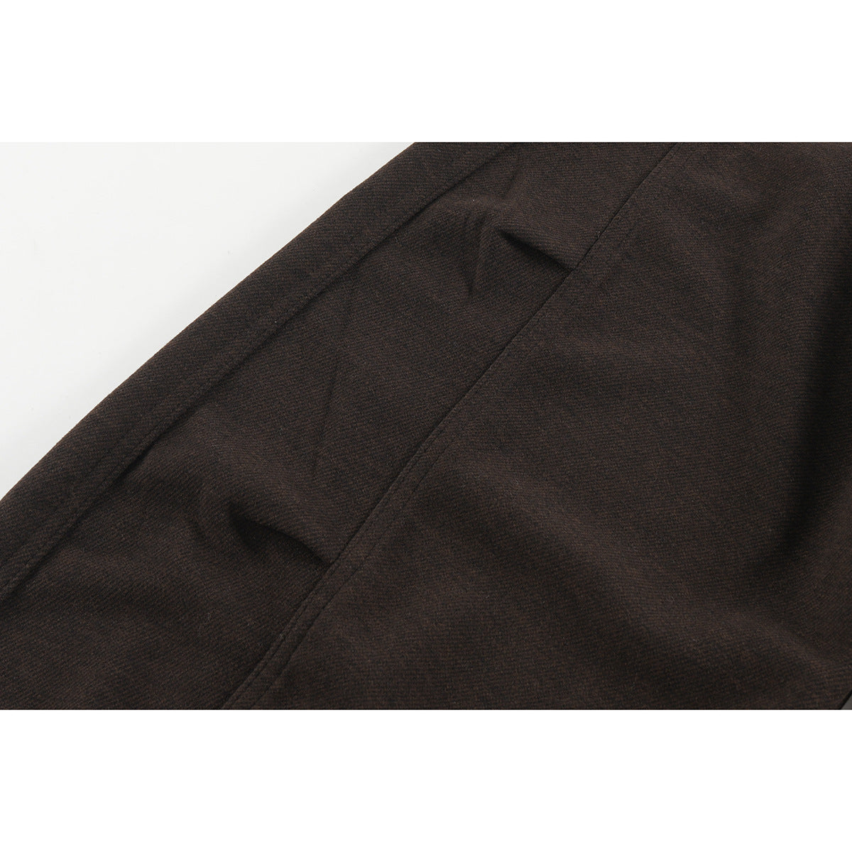 Close-up of dark brown trouser fabric, showing a side seam and pocket opening.