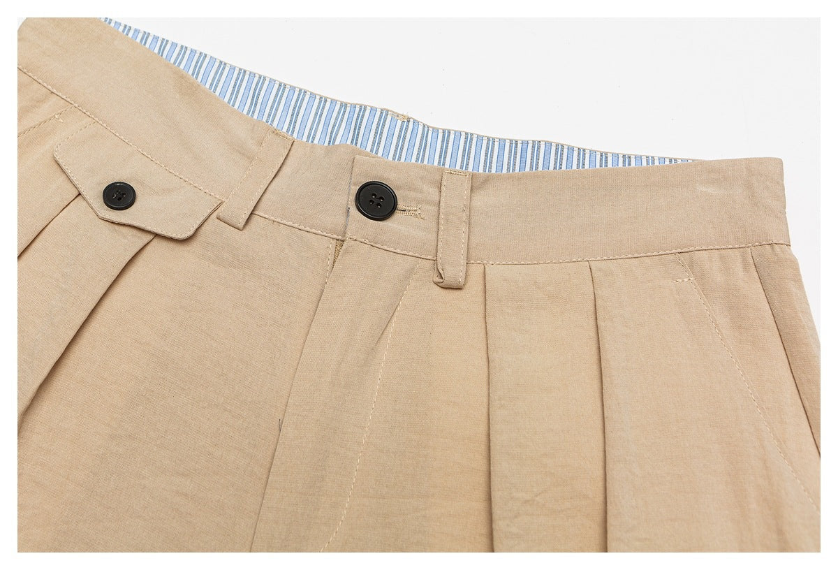 Front close-up of tan pleated trousers with black waistband buttons, belt loops, and blue striped lining.