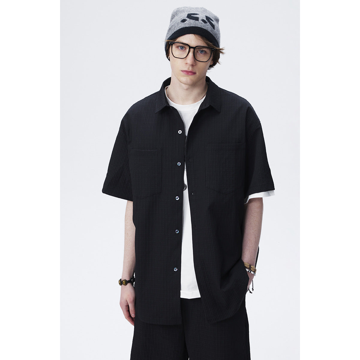 Front view of a model wearing an oversized black short-sleeve button-up shirt with two chest pockets over a white tee.