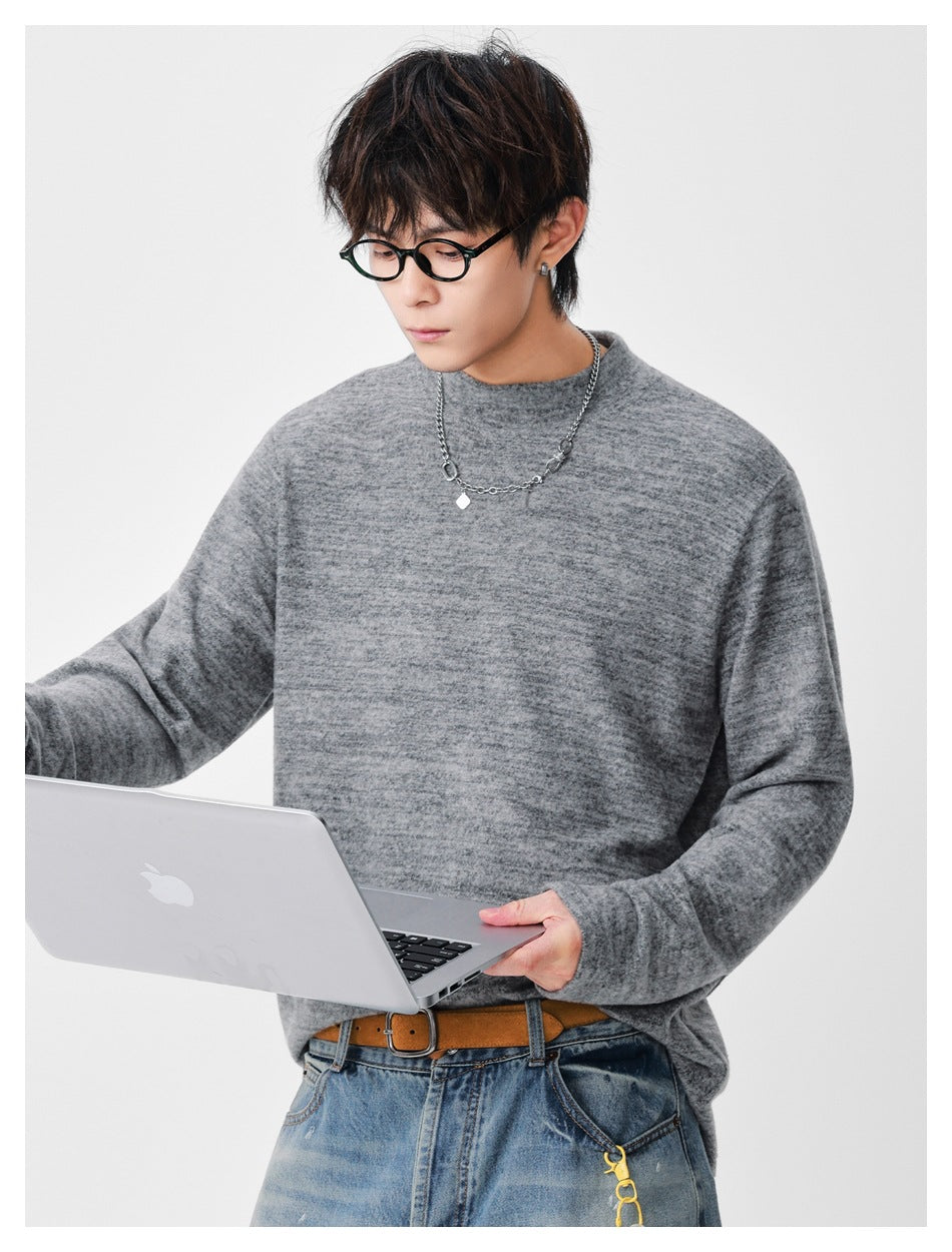 Model wearing a heather gray mock-neck long-sleeve top, holding a laptop that partly covers the front.