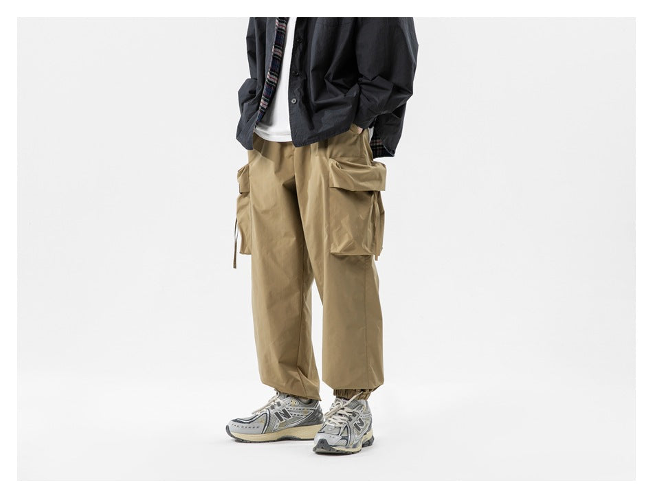 Front view of a model wearing loose tan cargo pants with oversized side pockets and gathered ankle cuffs.
