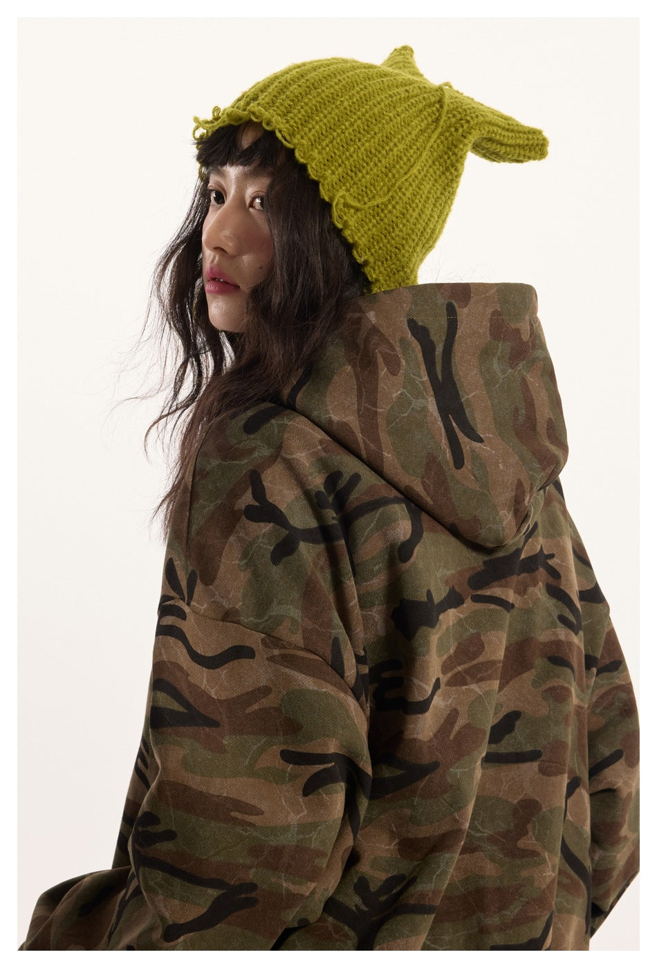 Side and back view of a model wearing an oversized camouflage hoodie with the hood up.
