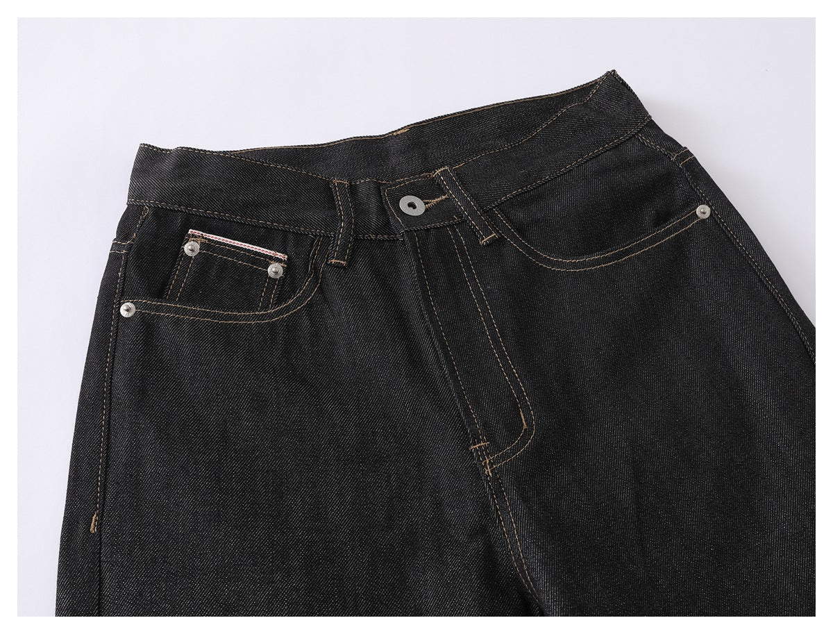 Close-up of the front waistband and pockets of black jeans with tan stitching and metal rivets.