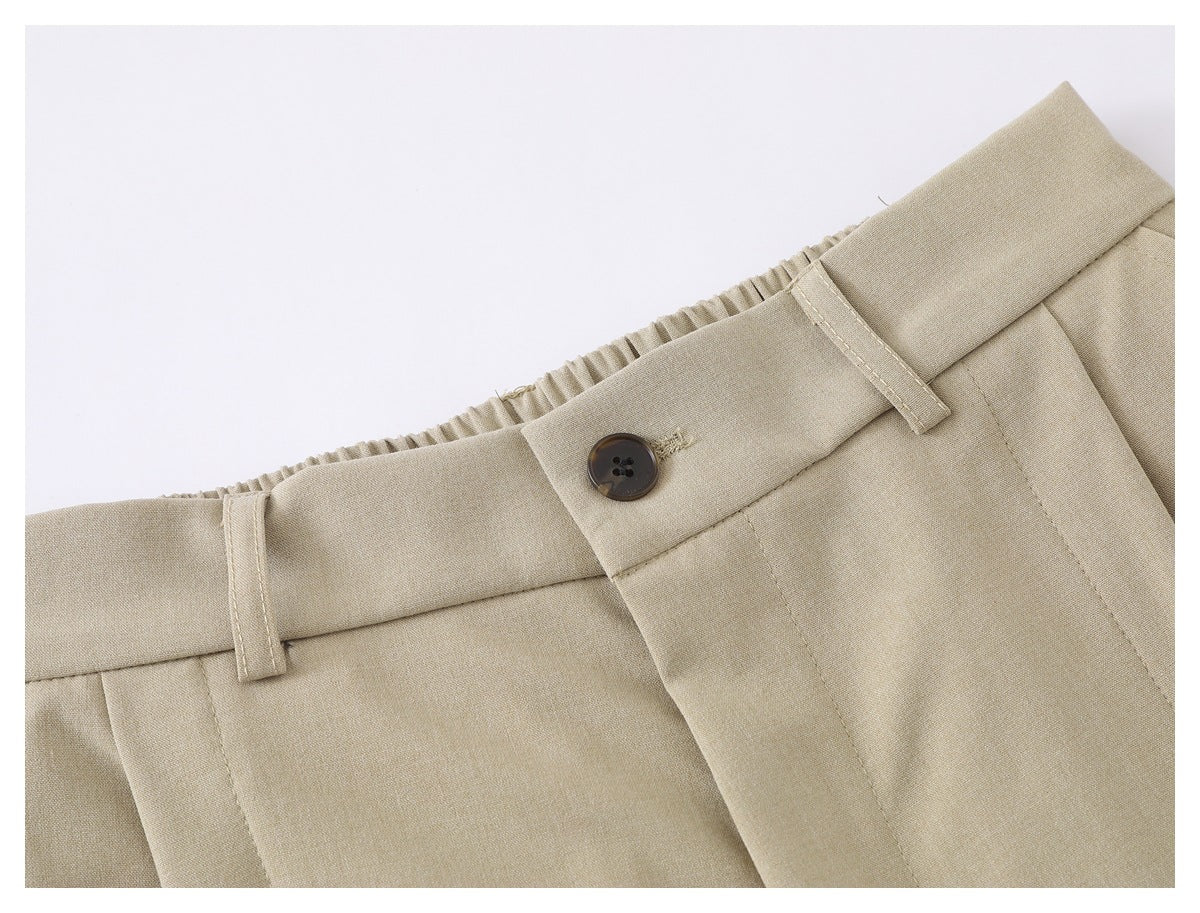 Close-up of beige trousers showing a dark button, belt loops, waistband, and front pleats.