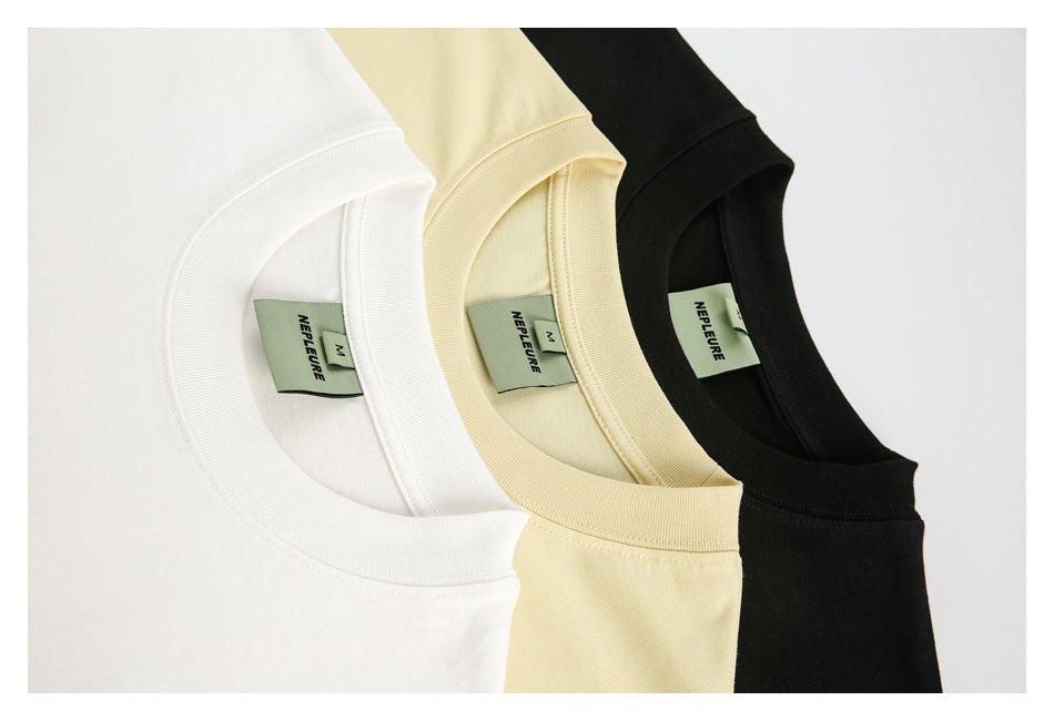 Close-up of white, pale yellow, and black crewneck shirts showing ribbed collars and sewn-in labels.