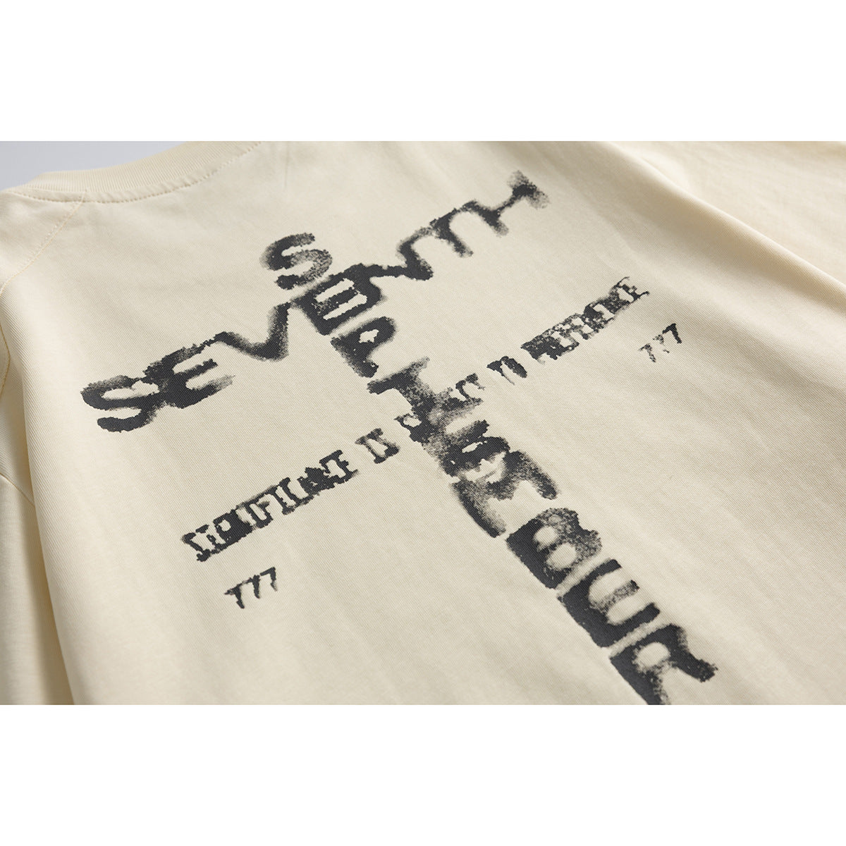 Close-up of a distressed black text graphic on the back of a cream T-shirt.