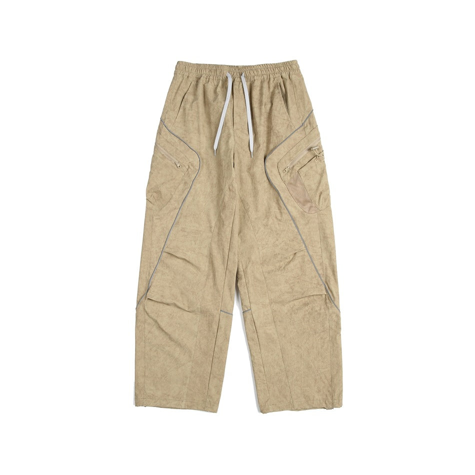 Front view of loose tan utility pants with an elastic drawstring waist, gray piping, and zippered side pockets.