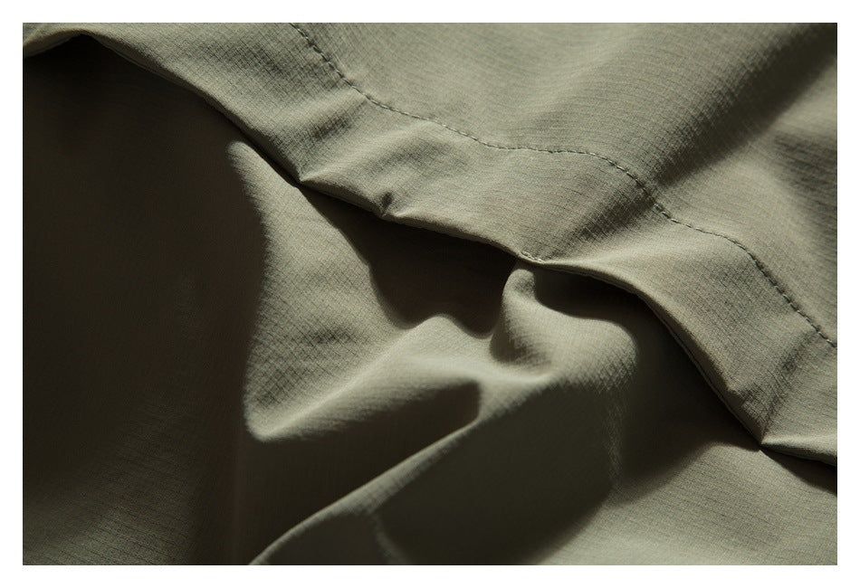 Close-up of an olive-gray garment seam and folded fabric, with stitching visible.