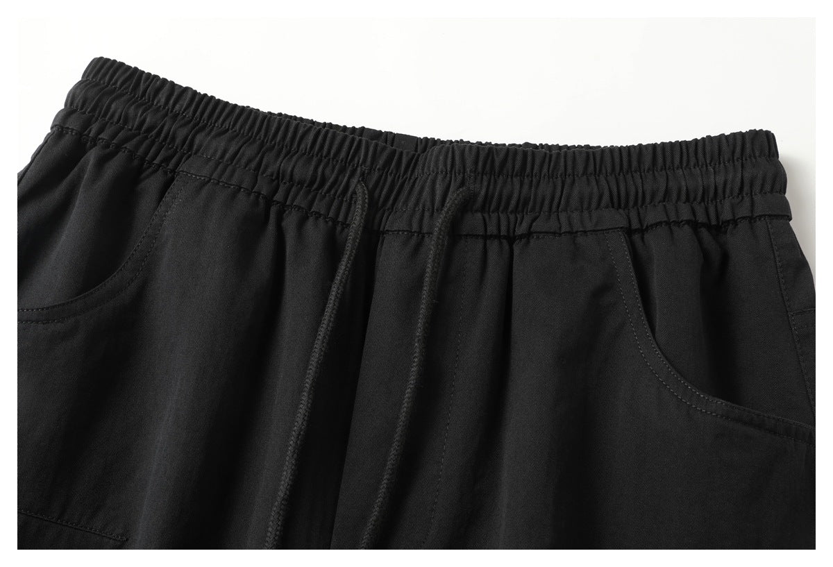 Close-up of black pants showing the gathered elastic waistband, drawstrings, and curved front pockets.