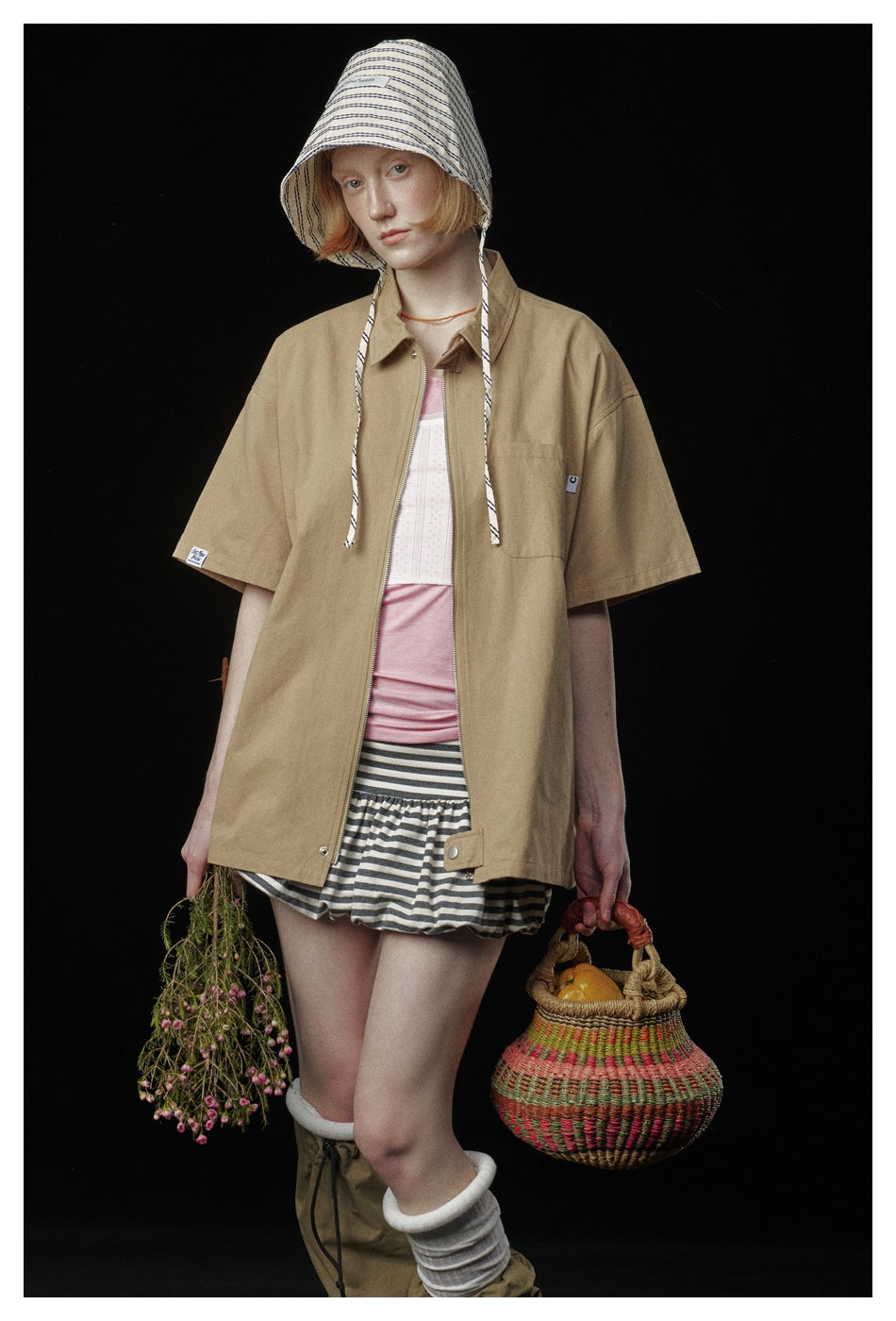 Front view of a model wearing a loose tan short-sleeve zip shirt with a collar and chest pocket.