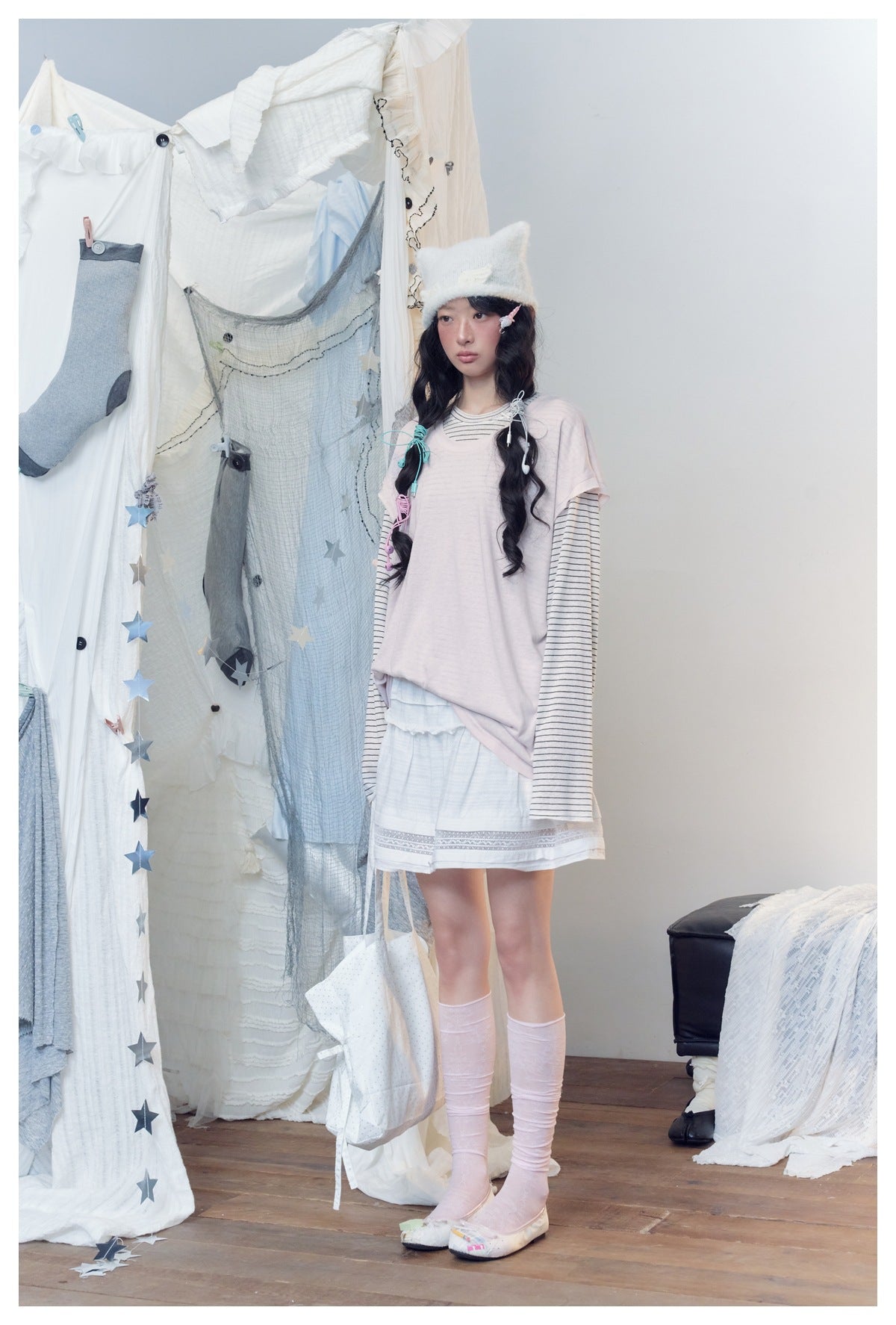 Model wearing pink layered striped top with white skirt and pink socks, standing at an angle with a tote bag