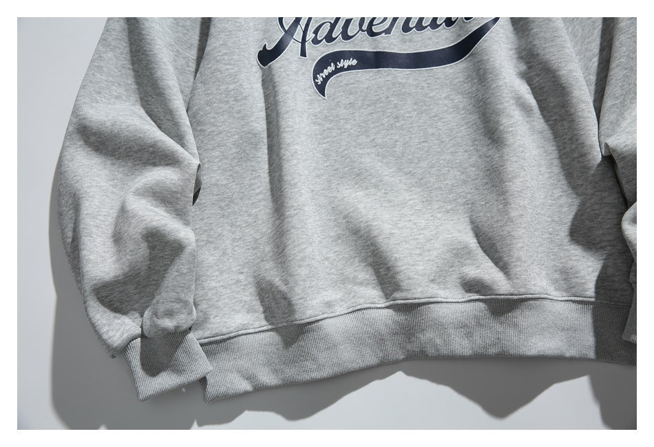 Close-up of a light gray sweatshirt’s front hem and ribbed cuff, with part of its navy script graphic visible.