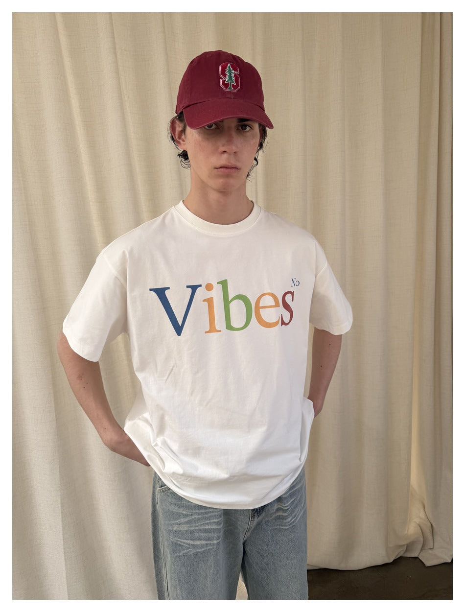 Closer view of a model wearing a white T-shirt with multicolored “Vibes No” lettering and a burgundy cap.