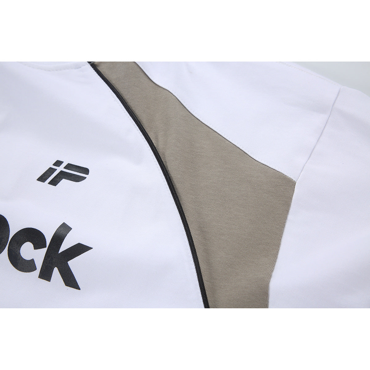 Close-up of a white shirt with a taupe panel, black piping, and part of a black chest graphic.